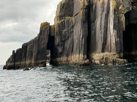 Jagged basalt sea caves and pillars rise from dark waters under a moody sky.