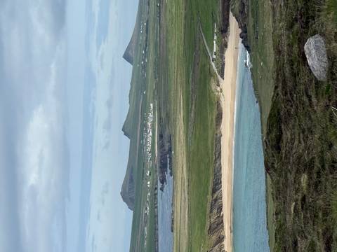 Rolling green peninsulas and sandy beaches are seen beneath distant pointed mountains.