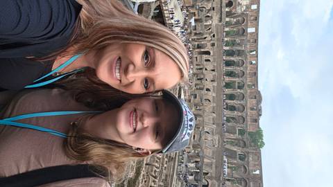 Selfie of two visitors inside Rome’s Colosseum with ancient stone tiers and crowds in the background.