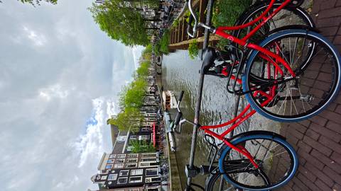 Amsterdam canal lined with historic gabled houses and red rental bikes in the foreground under dramatic clouds.