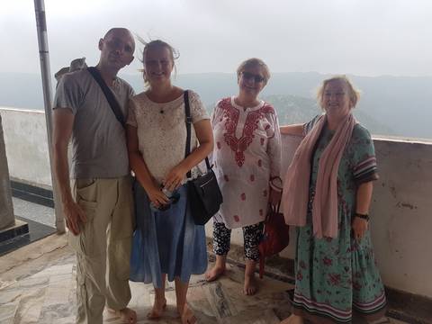 Four travelers posing together on a terrace with hazy mountains in background