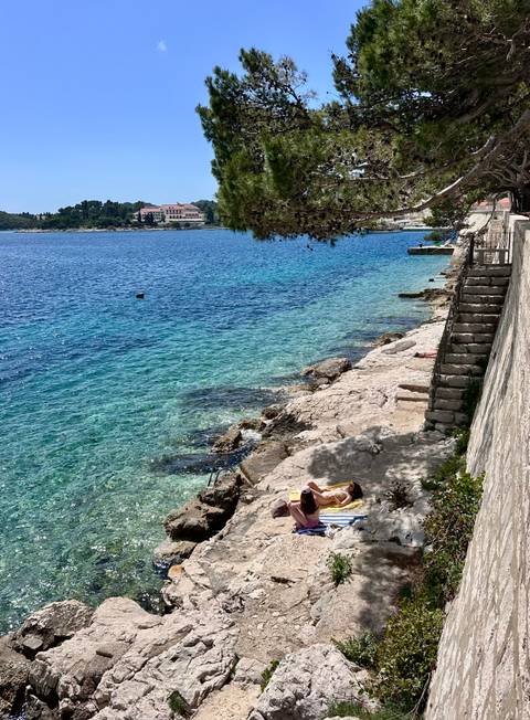 A sunbather relaxes on rocky steps beside crystal-clear Adriatic waters.