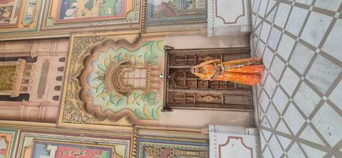 Woman in vibrant Rajasthani attire poses before an ornate carved doorway and painted arch in an Indian palace.