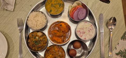 Traditional Indian thali platter featuring curries, rice, breads, sweets and fresh vegetables on a metal tray.