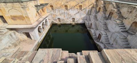 Historic stepwell with symmetrical staircases descending to a central green water pool.