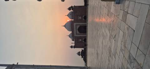 Silhouetted Mughal mosque within the Taj Mahal complex at sunrise with soft pastel sky.