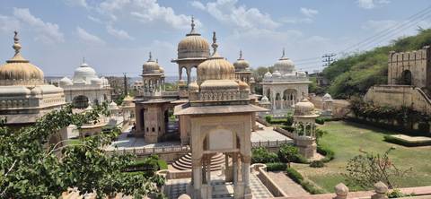 Marble cenotaphs and domed pavilions surrounded by manicured gardens beneath a bright sky.