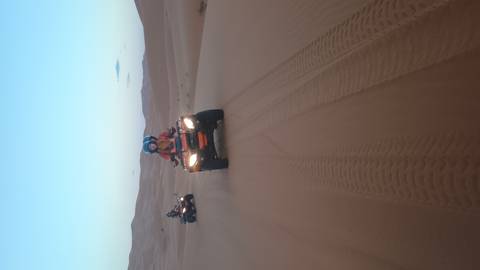 Two riders power quad bikes across soft desert sand leaving curving tyre tracks behind.