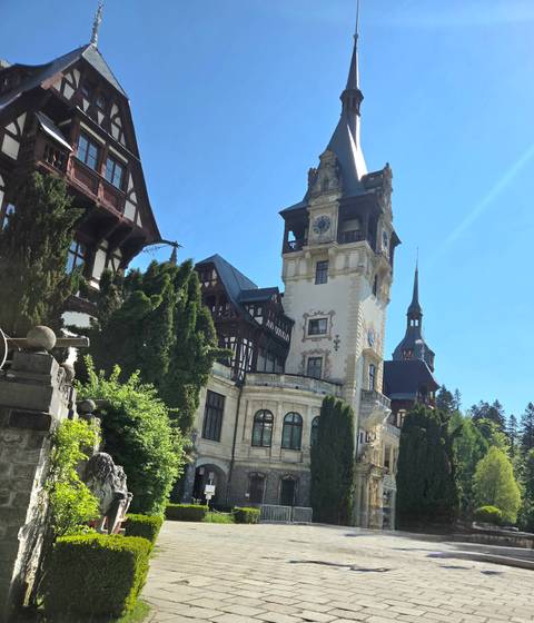 Neo-Renaissance Peles Castle rises amid evergreen forests under a bright Carpathian sky.