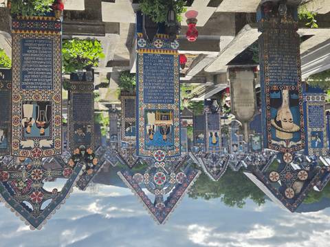 Rows of ornate blue and red carved crosses extend through the Merry Cemetery with hills behind.