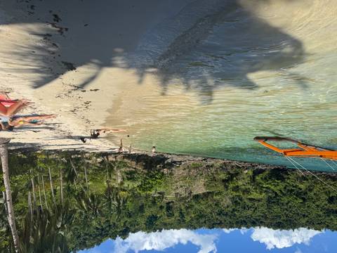Secluded tropical beach with clear turquoise water, people relaxing on the sand and a banca boat offshore
