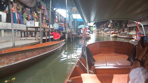 View from inside a boat weaving through narrow lanes of a lively floating market in Thailand.