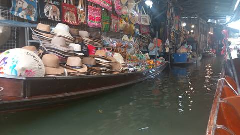 Merchandise-laden boat selling hats and souvenirs drifting through a covered floating market alley.