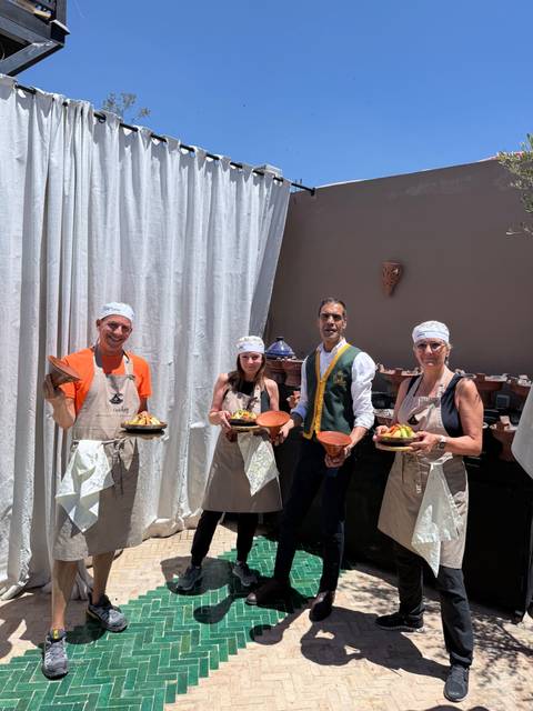 Cooking class participants holding tagines and dishes while posing with their instructor.