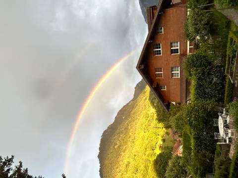 Double rainbow arching over an alpine valley with wooden chalet and green mountainside.