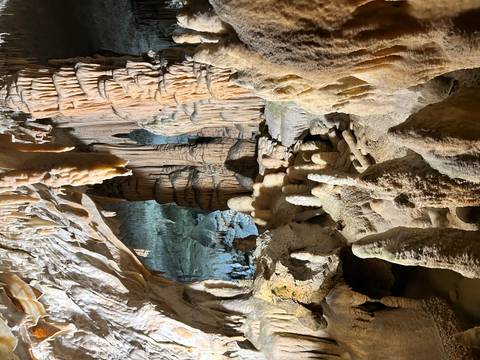 Dramatic limestone cave interior with stalactites and stalagmites lit by warm lights.