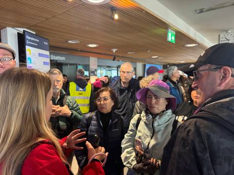 Travellers listen to a guide inside a busy alpine train station terminal.