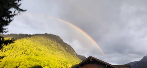 Faint double rainbow arcs over a forested mountain ridge at dusk.