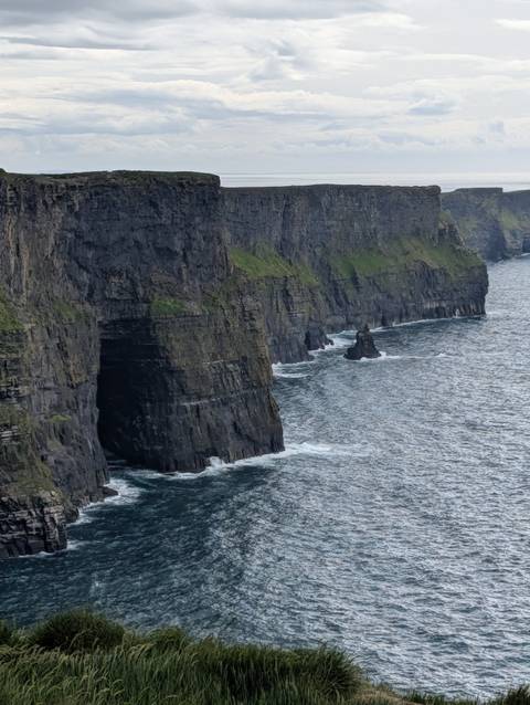 Dramatic sheer sea cliffs with dark rock faces rise above choppy Atlantic waters.