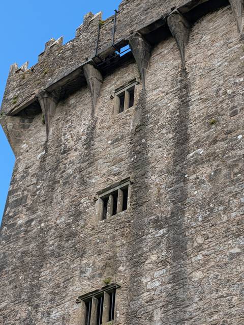 Close-up of rough stone castle wall with narrow medieval windows against blue sky.