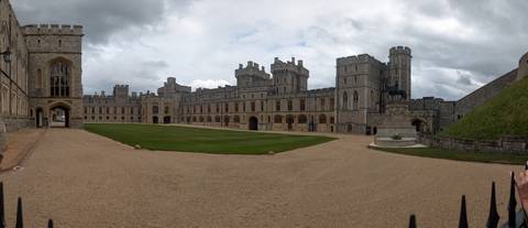 Wide courtyard panorama of Windsor Castle with towers surrounding manicured lawn.