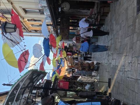 Narrow bazaar street decorated with colorful hanging umbrellas and shoppers walking