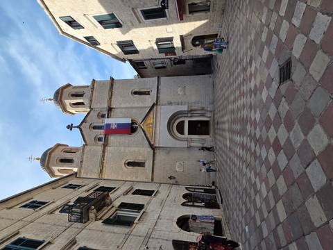 Stone-faced Serbian Orthodox church fronting a tiled square within medieval walls