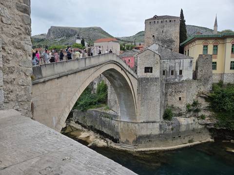 Iconic single-arch stone bridge of Mostar spanning emerald river with tourists on top