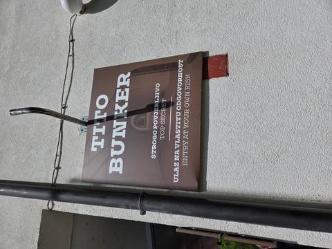 Brown sign on wall reading 'Tito Bunker' with multilingual warnings