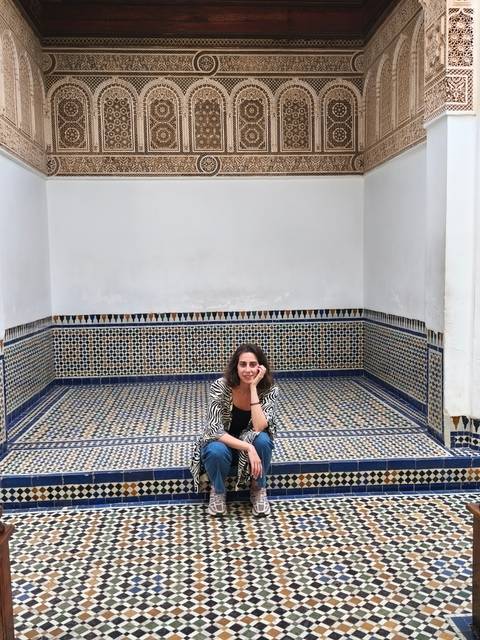 A woman sits in a beautifully tiled Moroccan alcove with intricate mosaic patterns.