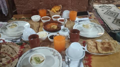 A traditional Moroccan breakfast spread featuring juices, breads, and tagine on a low table.