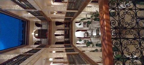 An ornate multi-storey riad interior with patterned tiles, arches and soft evening lighting.