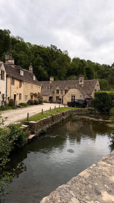 A tranquil scene of honey-coloured cottages and a stone bridge beside a reflective stream in a rural village.