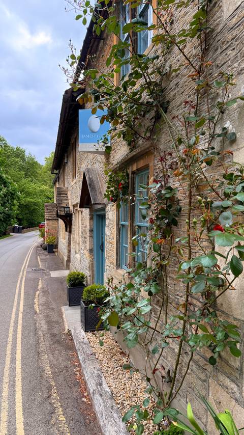 Close-up of a Cotswold cottage with blue door and blooming roses climbing its stone façade.