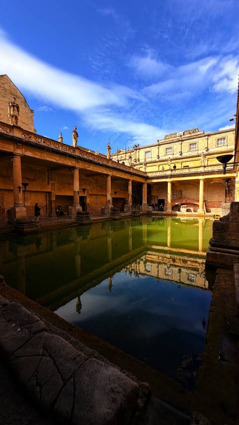 The historic Roman Baths feature steaming green water surrounded by sandstone columns and visitors.