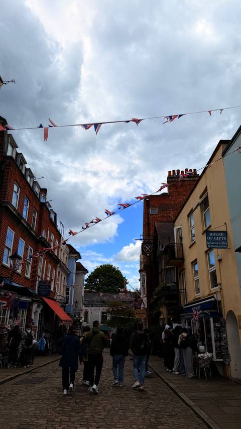 Colourful Union Jack bunting stretches above a brick-lined street under a patchy sky.
