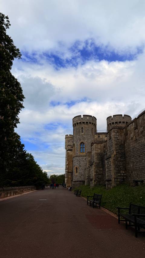 Stone towers of Windsor Castle rise against a partly cloudy blue sky.