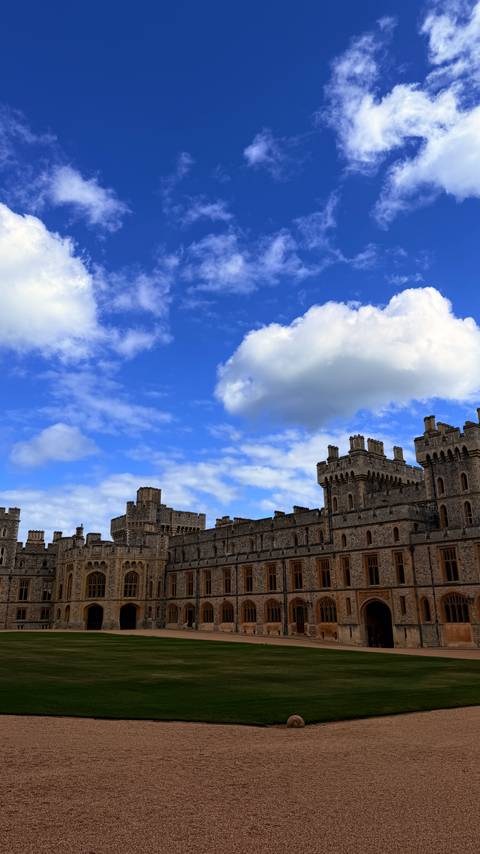 Extended view of Windsor Castle’s battlements set beneath vivid blue sky and fluffy clouds.