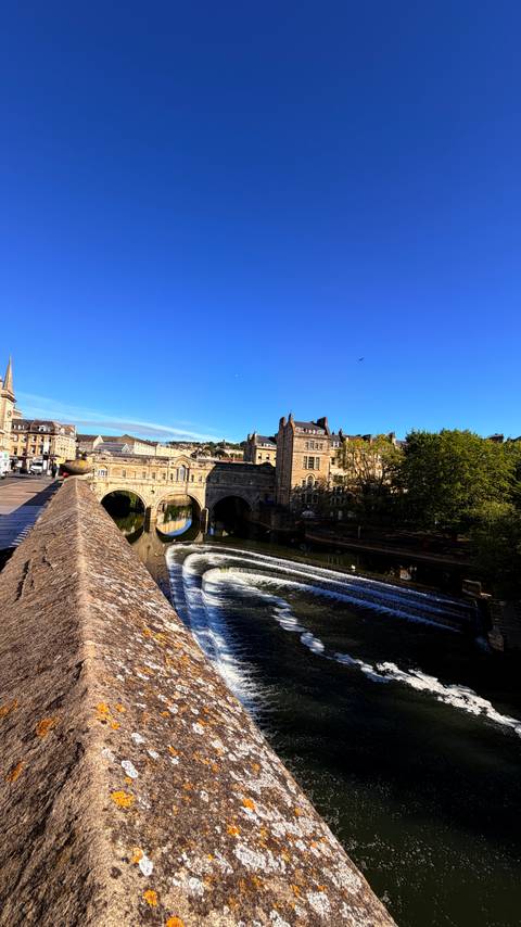 Bath’s Pulteney Bridge and weir curve gracefully over the River Avon on a sunny morning.