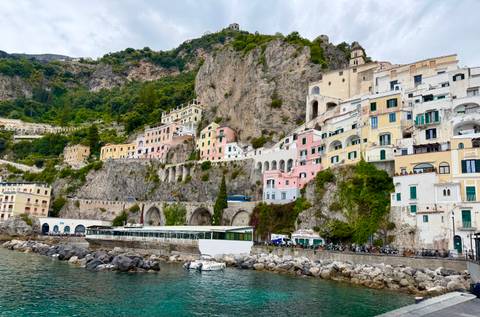 Colorful hillside houses cling to dramatic limestone cliffs above turquoise water along the Amalfi Coast.