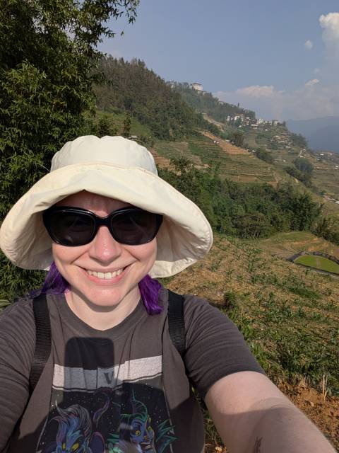 Smiling trekker wearing sun hat and sunglasses takes a selfie with Sapa rice terraces behind.