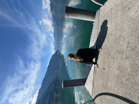 Young woman sitting on a dock gazing over a tranquil alpine lake with mountains mirrored in the water.