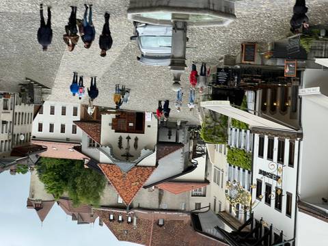 Cobblestoned village square with historic buildings and clusters of tourists strolling and dining outdoors.