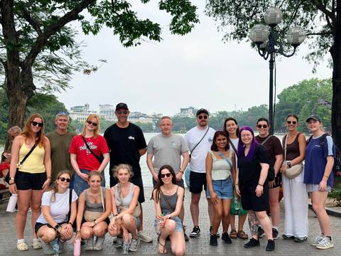 Large tour group posing together in an urban park with lake and city skyline in the background.