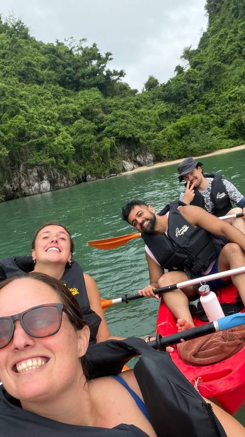 Smiling friends in life jackets kayaking on emerald waters beside limestone cliffs.