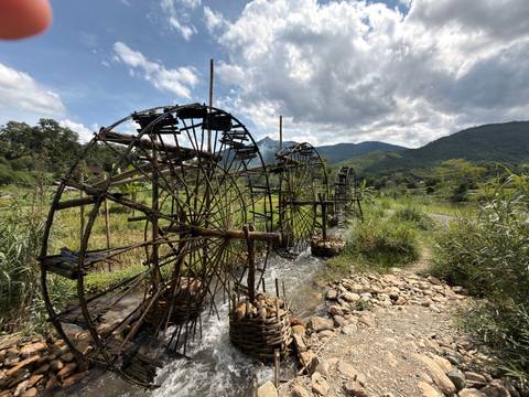 Series of rustic bamboo water wheels channel mountain stream water beside lush green valley.