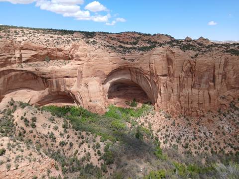 A sweeping view of a massive natural sandstone arch and surrounding desert canyon walls under a clear blue sky.