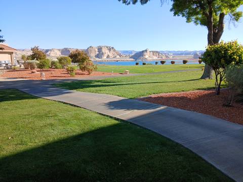 Grassy hotel lawn and walkway leading to distant sandstone cliffs and a blue lake.