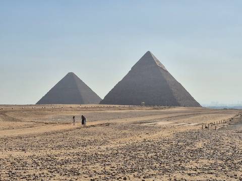Two prominent pyramids rising above the desert sands under a hazy blue sky.