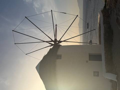 Silhouetted traditional windmill at sunset with golden light reflecting on the sea.